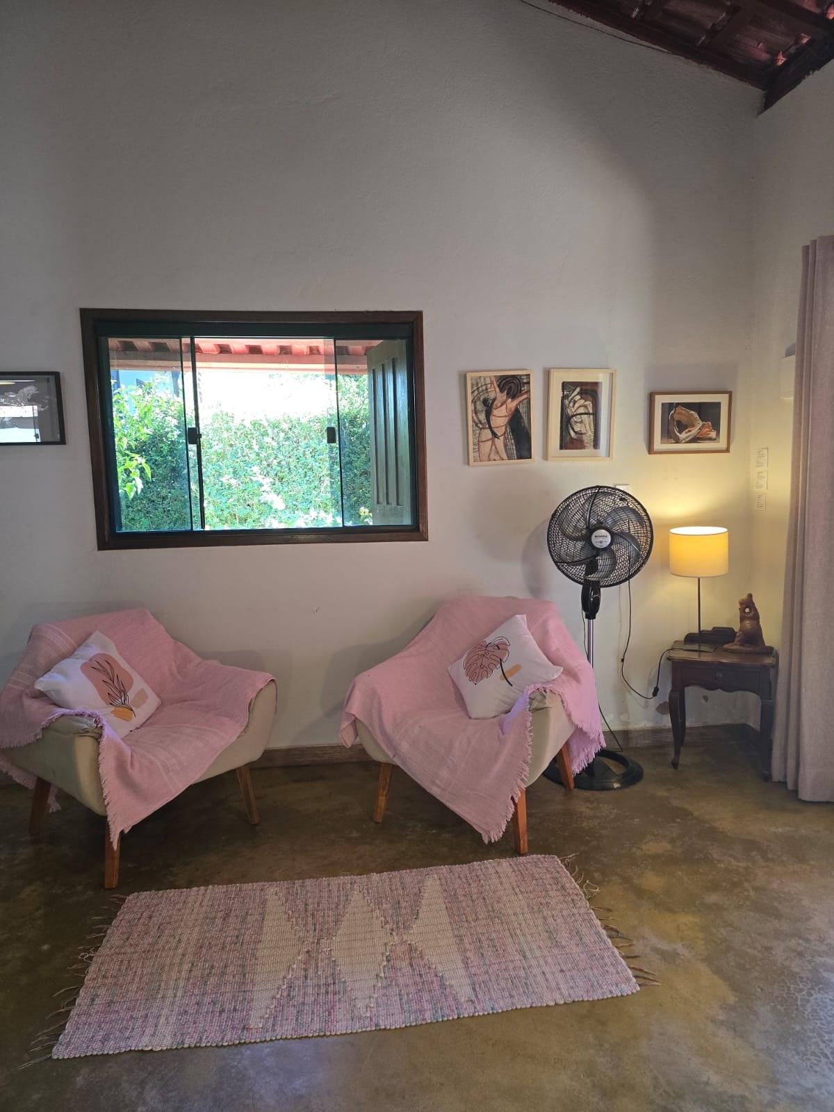 Poltronas da sala, com quadros na parede e ventilador